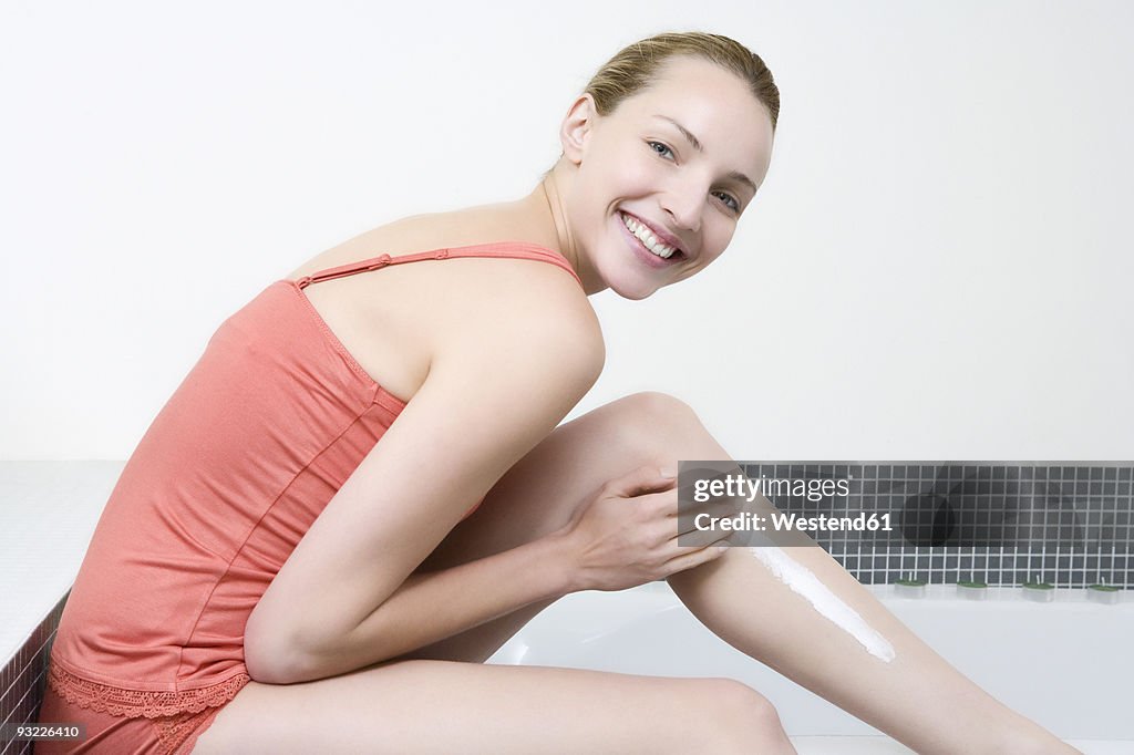 Young woman applying cream on legs