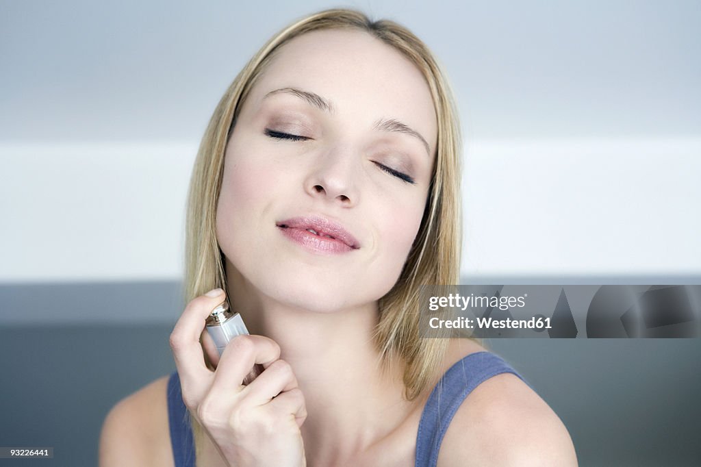 Young woman spraying perfume on neck, portrait