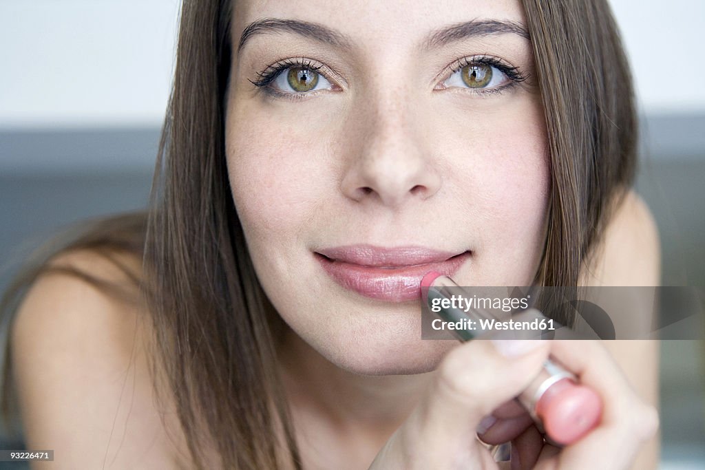 Young woman applying lipstick, portrait, close-up