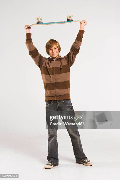 teenage boy (13-14) holding skateboard over head, smiling - figure skater stockfoto's en -beelden