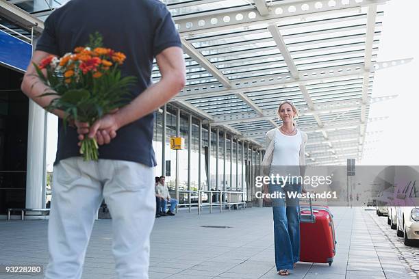 germany, leipzig-halle, airport, woman with suitcase, man holding flowers - hands behind back stockfoto's en -beelden