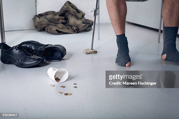 germany, plastic cup and coins on floor, shoeless person in background, low section - mareen fischinger stock-fotos und bilder