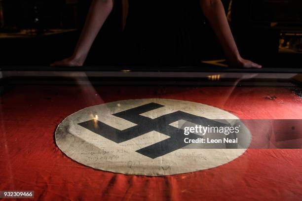 Gallery assistant poses with a captured Nazi swastika flag, signed by original members of the SAS, listing their missions in Africa during World War...