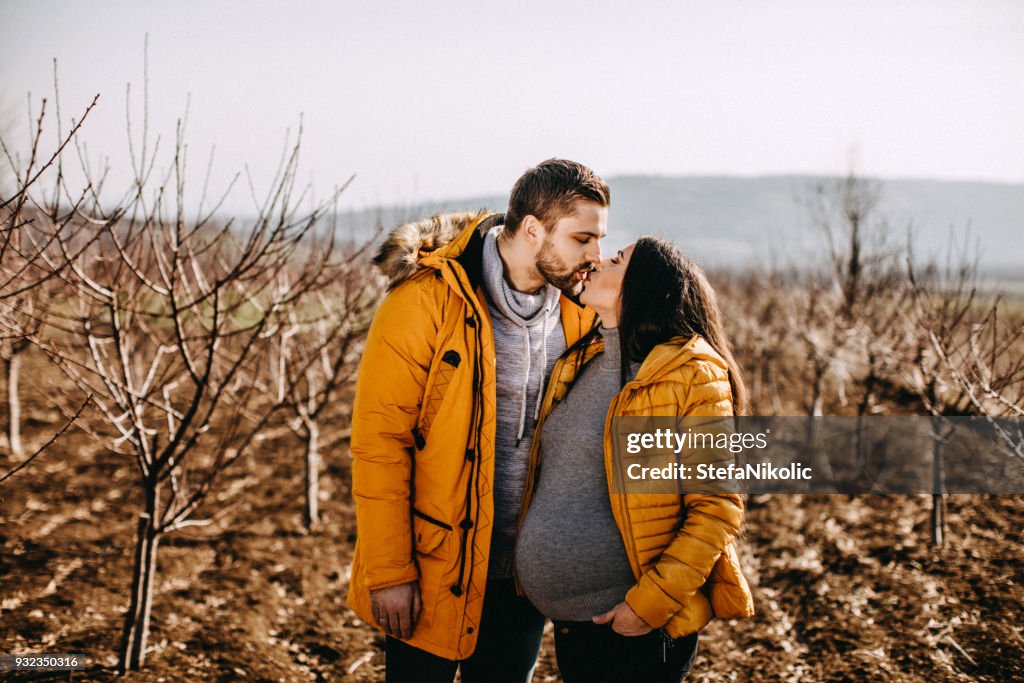 Happy pregnant couple kissing on the sun
