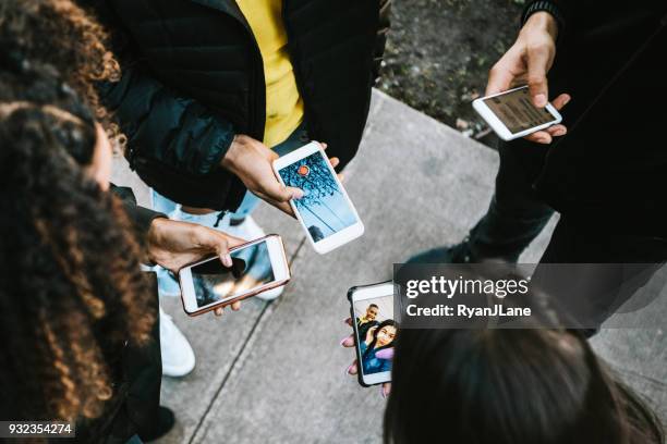 group of young adults looking at phone - sociaal netwerk stock pictures, royalty-free photos & images