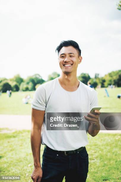 schöne chinesische kerl mit smartphone im park - chinese model stock-fotos und bilder