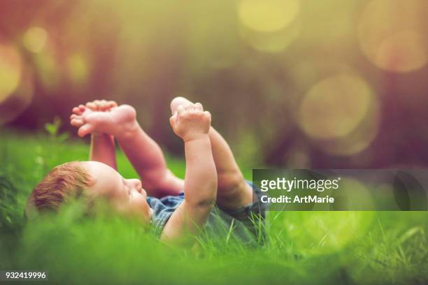niedliche baby spielt mit seinen beinen auf dem rasen - junge barfuß stock-fotos und bilder