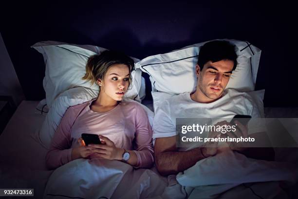 téléphone mobile addiction - femme jalouse est furtivement son mari d’envoyer des sms dans le lit - regarder à la dérobée photos et images de collection