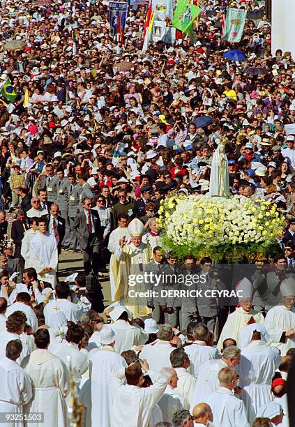 Pope John Paul II waves to the cheering crowd 12 May 1991 as he walks behind the statue of the Virgin of Fatima prior to celebrates a mass in the...