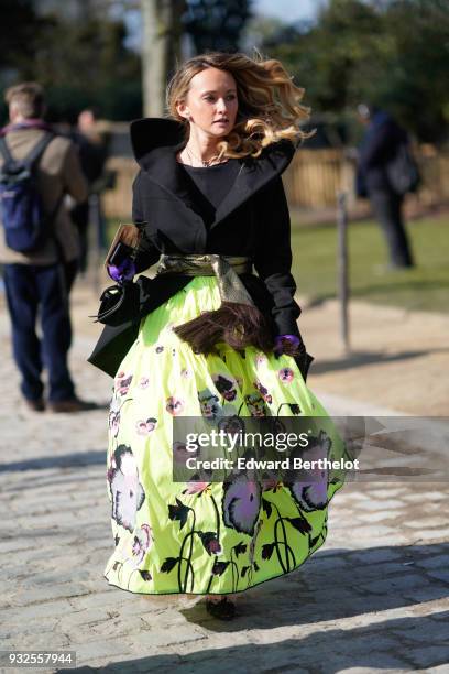 Guest wears a black boatneck top, a black shirt with a large collar, a golden fringe scarf belt, a green large skirt with pansies pattern , during...