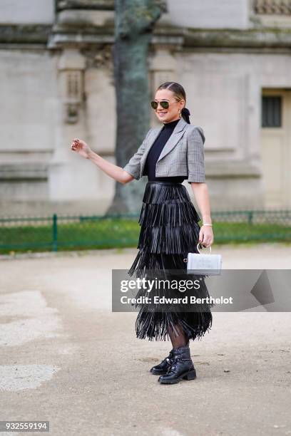 Guest wears sunglasses, a highneck top, large creole earrings, a grey prince-of-wales checkered bolero jacket, a black fringe long skirt , a grey...
