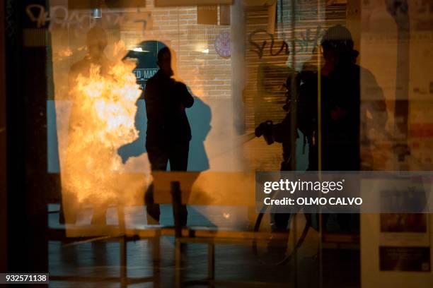 Firefighters try to extinguish a fire during a protest following the death of a street vendor at Lavapies district in Madrid on March 15, 2018....