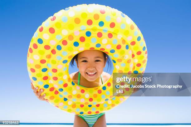 eurasian girl holding inflatable ring on beach - fille maillot photos et images de collection