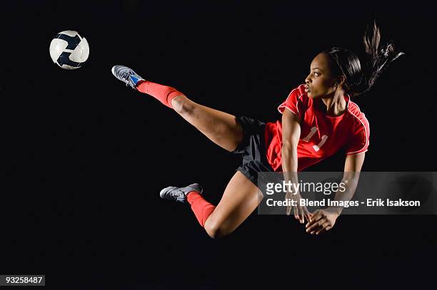 mixed race soccer player kicking soccer ball in mid-air - woman football stock-fotos und bilder