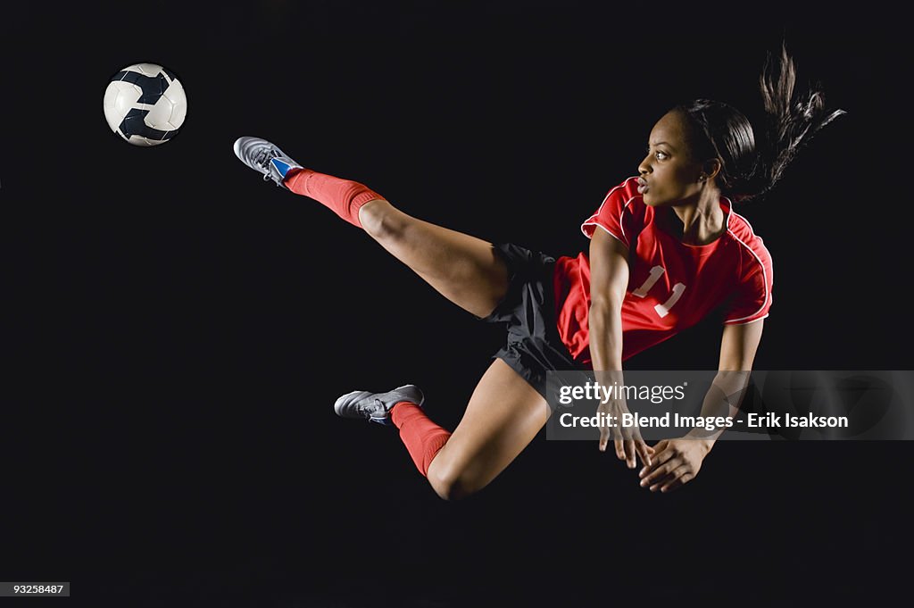 Mixed race soccer player kicking soccer ball in mid-air