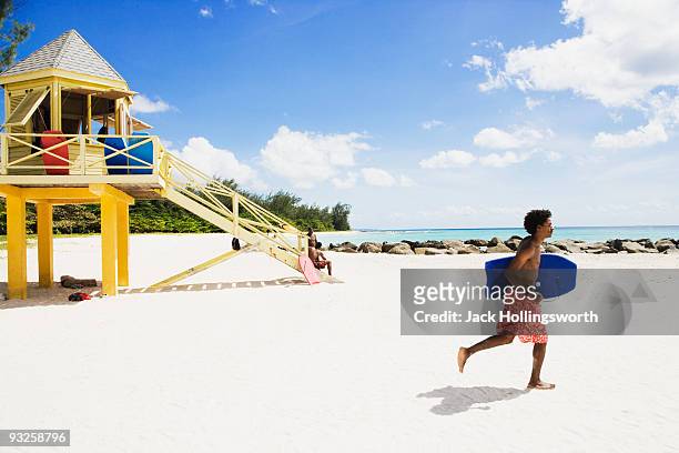 african man running with body board on beach - barbados stock pictures, royalty-free photos & images