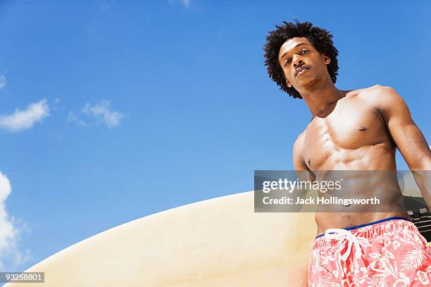 serious african man holding surfboard - black people in bathing suits stock pictures, royalty-free photos & images