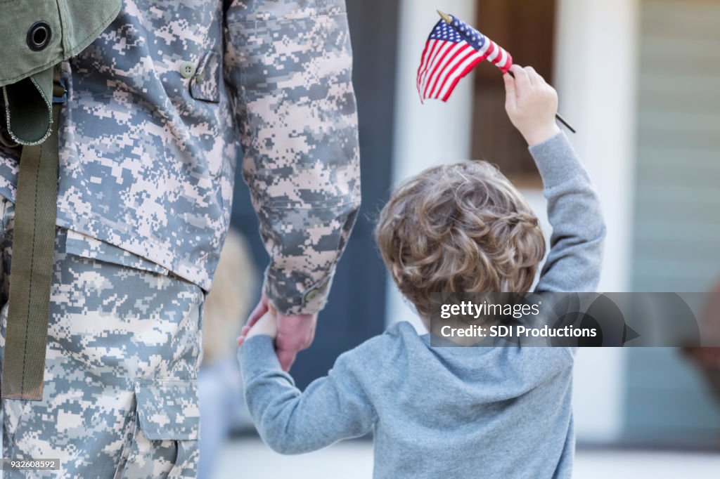 Vista posterior de niño cogidos de la mano con papá militar