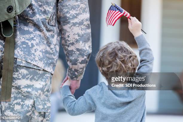 achteraanzicht van jongen hand in hand met militaire papa - terugkomdag stockfoto's en -beelden