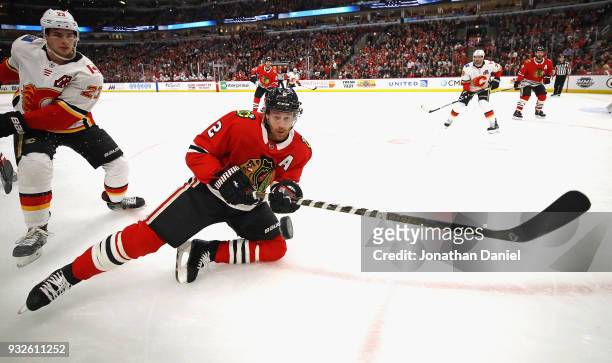 Duncan Keith of the Chicago Blackhawks reaches for the puck from one knee in front of Sean Monahan of the Calgary Flames at the United Center on...