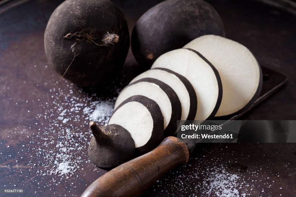 Whole and sliced black radish and an old cleaver on rusty ground