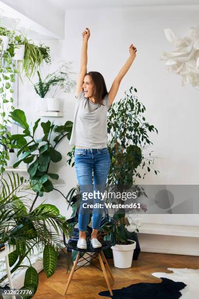 young woman standing on chair in a room cheering - standing on chair stockfoto's en -beelden