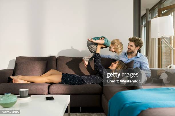 happy parents playing with son on sofa at home - playing sofa stock-fotos und bilder