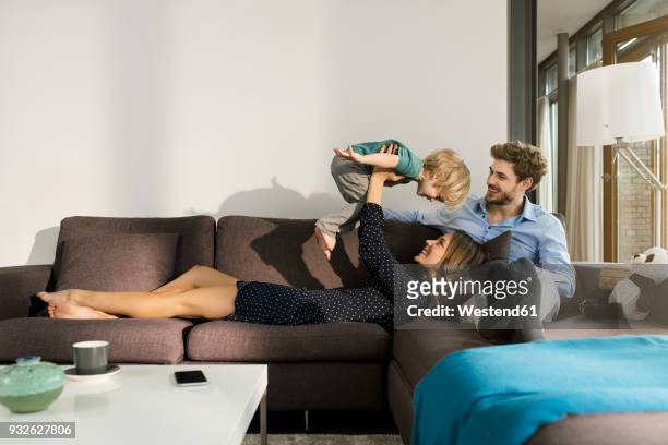 happy parents playing with son on sofa at home - playing sofa stockfoto's en -beelden