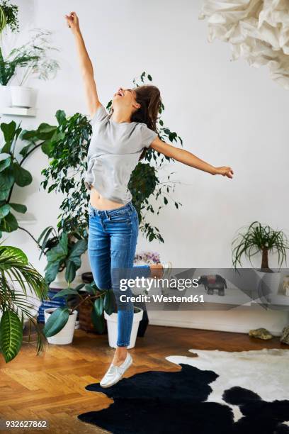 exuberant young woman jumping in a room - eco champions stock pictures, royalty-free photos & images