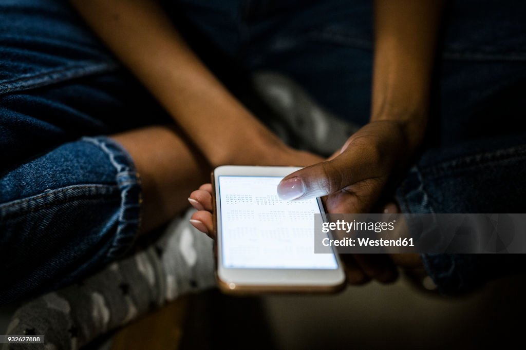 Young woman sitting at home, holding illuminated smartphone at night