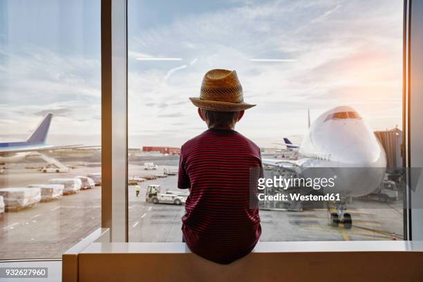 boy wearing straw hat looking through window to airplane on the apron - airplane travel stock-fotos und bilder