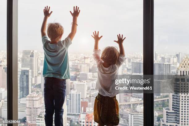 thailand, bangkok, boy and little girl looking through window at cityscape - rear view hand window stockfoto's en -beelden