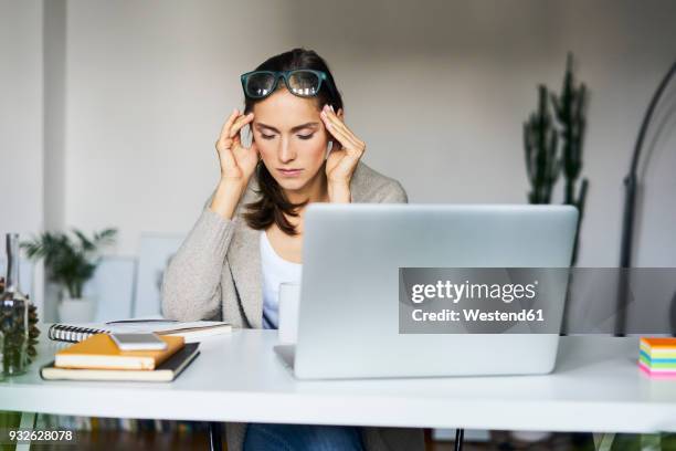 young woman at home with laptop on desk touching her temples - attentif photos et images de collection