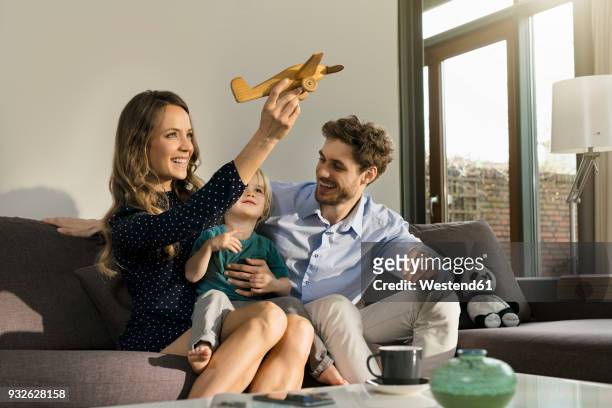 happy parents and son playing with wooden toy plane on sofa at home - the house of flaunt oscar retreat hosted by manuel day 1 stockfoto's en -beelden