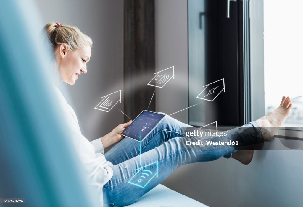 Woman sitting in office, using digital tablet to remote-control his smart home