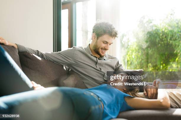 affectionate couple smiling at each other on sofa at home - comfortable couple stock pictures, royalty-free photos & images