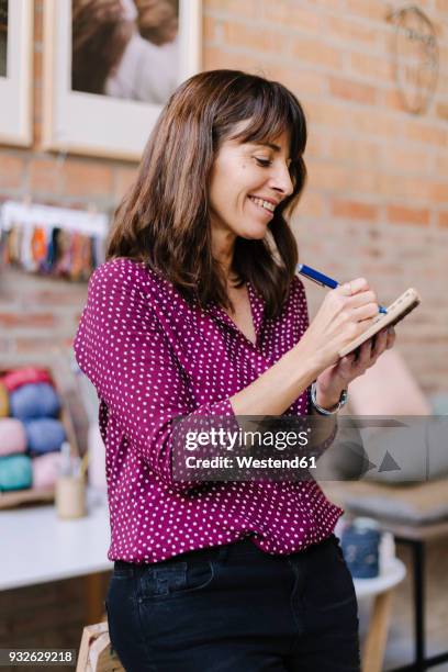 smiling woman in knitting studio taking notes - 50s woman writing at table imagens e fotografias de stock