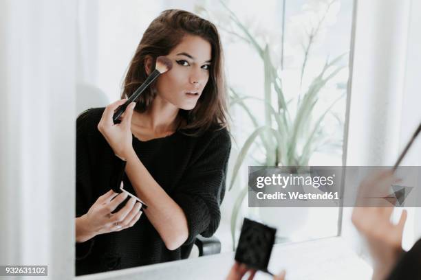 mirror image of young woman applying makeup - woman applying blush stock pictures, royalty-free photos & images