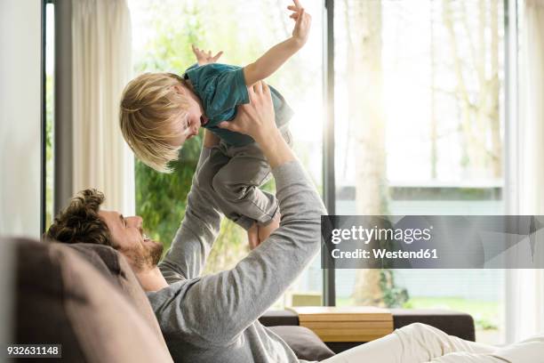 happy father playing with son on sofa at home - hacer el avión fotografías e imágenes de stock