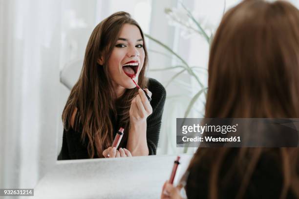 mirror image of young woman applying lipstick - trucco per il viso foto e immagini stock