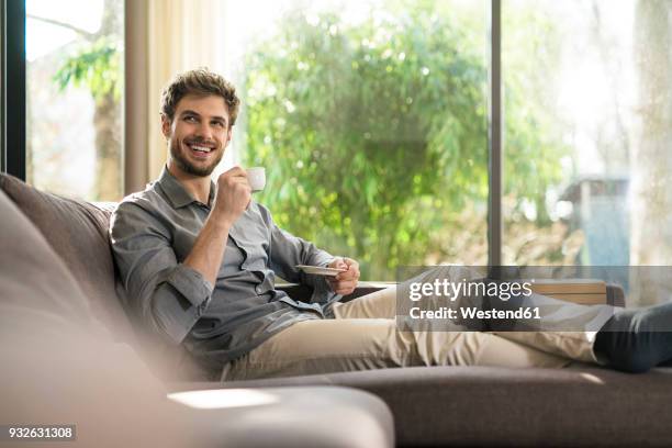 laughing man relaxing on couch at home drinking coffee - sofa modern stock-fotos und bilder