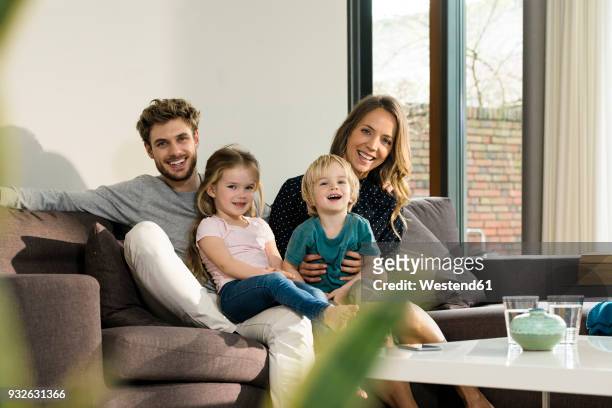 portrait of happy family sitting on sofa at home - auslachen blick in die kamera stock-fotos und bilder