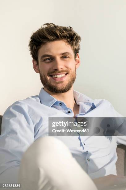 portrait of smiling young man sitting on couch - pelo facial imagens e fotografias de stock