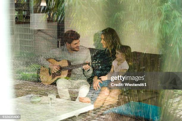 happy parents and daughter playing guitar on sofa at home - bamboo guitar stock pictures, royalty-free photos & images
