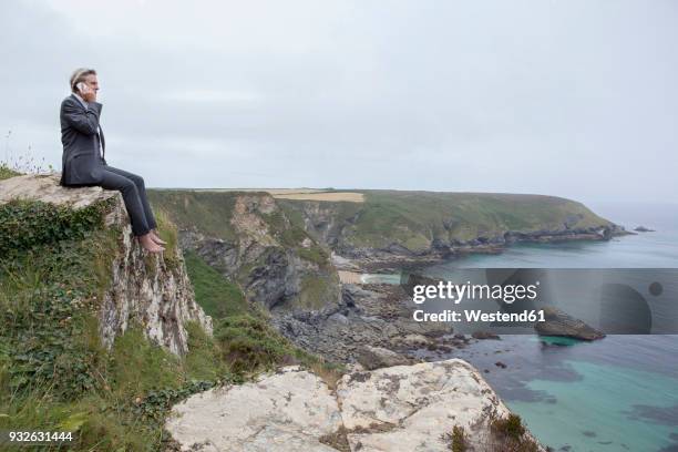 uk, cornwall, gwithian, businessman sitting at the coast talking on cell phone - gwithian ストックフォトと画像