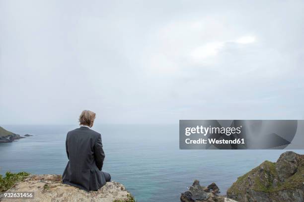 uk, cornwall, gwithian, businessman sitting at the coast looking at view - gwithian ストックフォトと画像