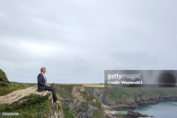 uk, cornwall, gwithian, businessman sitting at the coast using laptop - gwithian foto e immagini stock