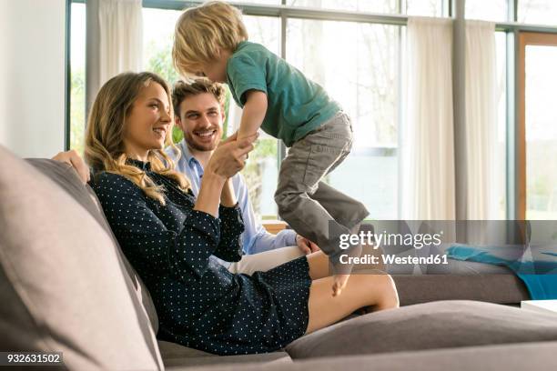 happy parents playing with son on sofa at home - three people on couch stock pictures, royalty-free photos & images