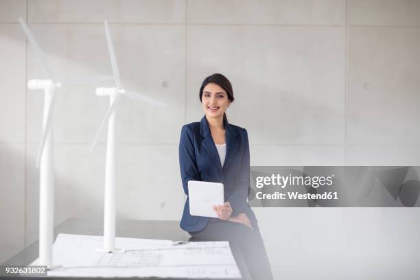 portrait of smiling young woman with blueprint, wind turbine models and tablet in office - asian and indian ethnicities imagens e fotografias de stock