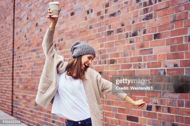 happy woman with coffee to go singing and dancing on the street - sombrero marrón fotografías e imágenes de stock